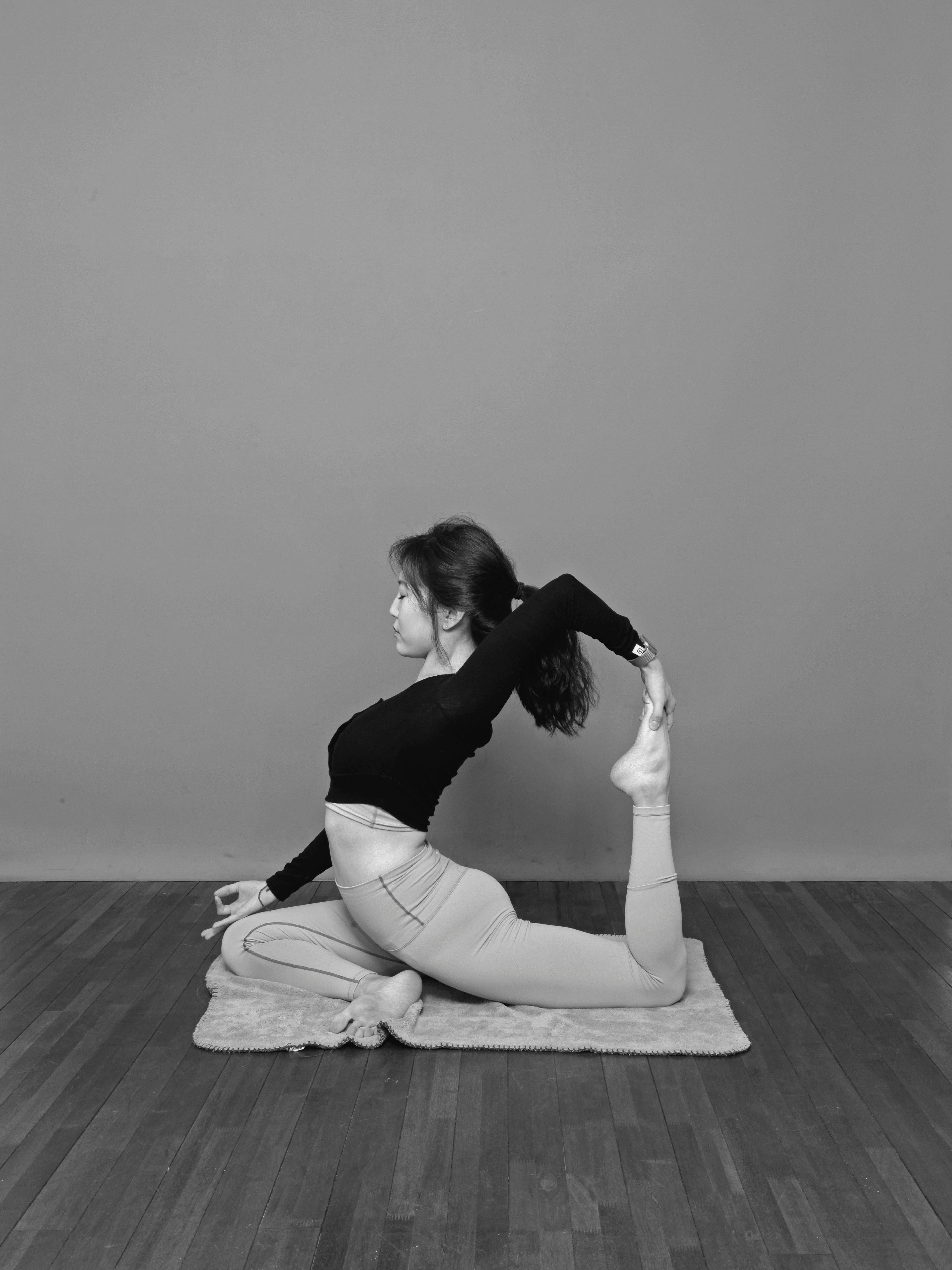 ヨガ講師 Asana のモノクロポートレート、横向きに座って後ろ手に足首を持つポーズ