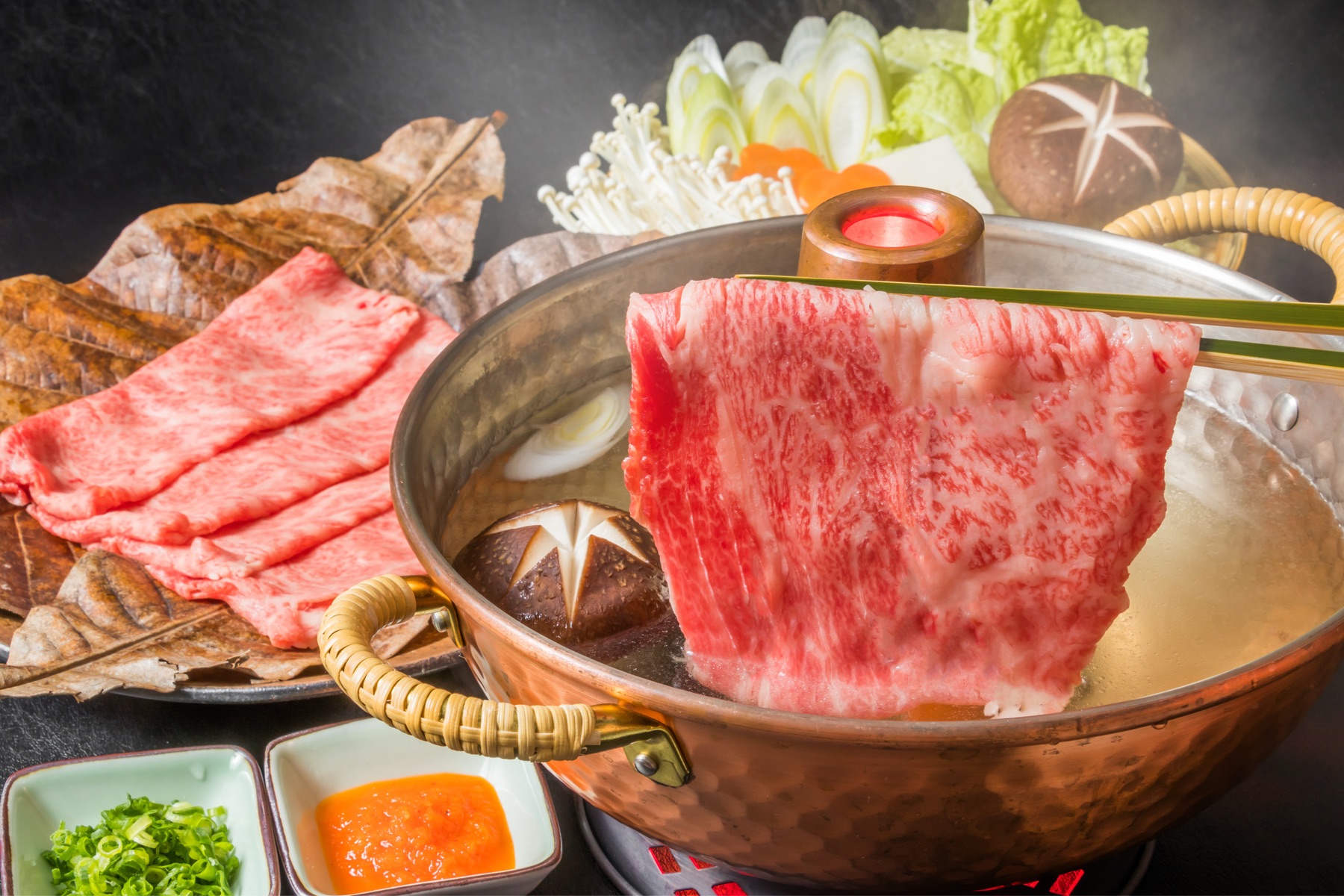 銅鍋の出汁に、箸でつまんだ薄切り肉をくぐらせる